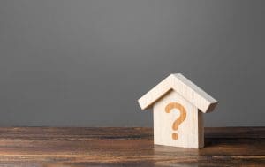 A wooden house with a question mark on it on a wooden table.